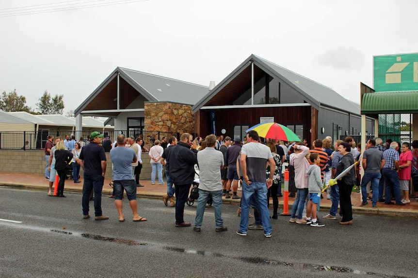 A large group of people are gathered outside a brand new pub on an overcast day.