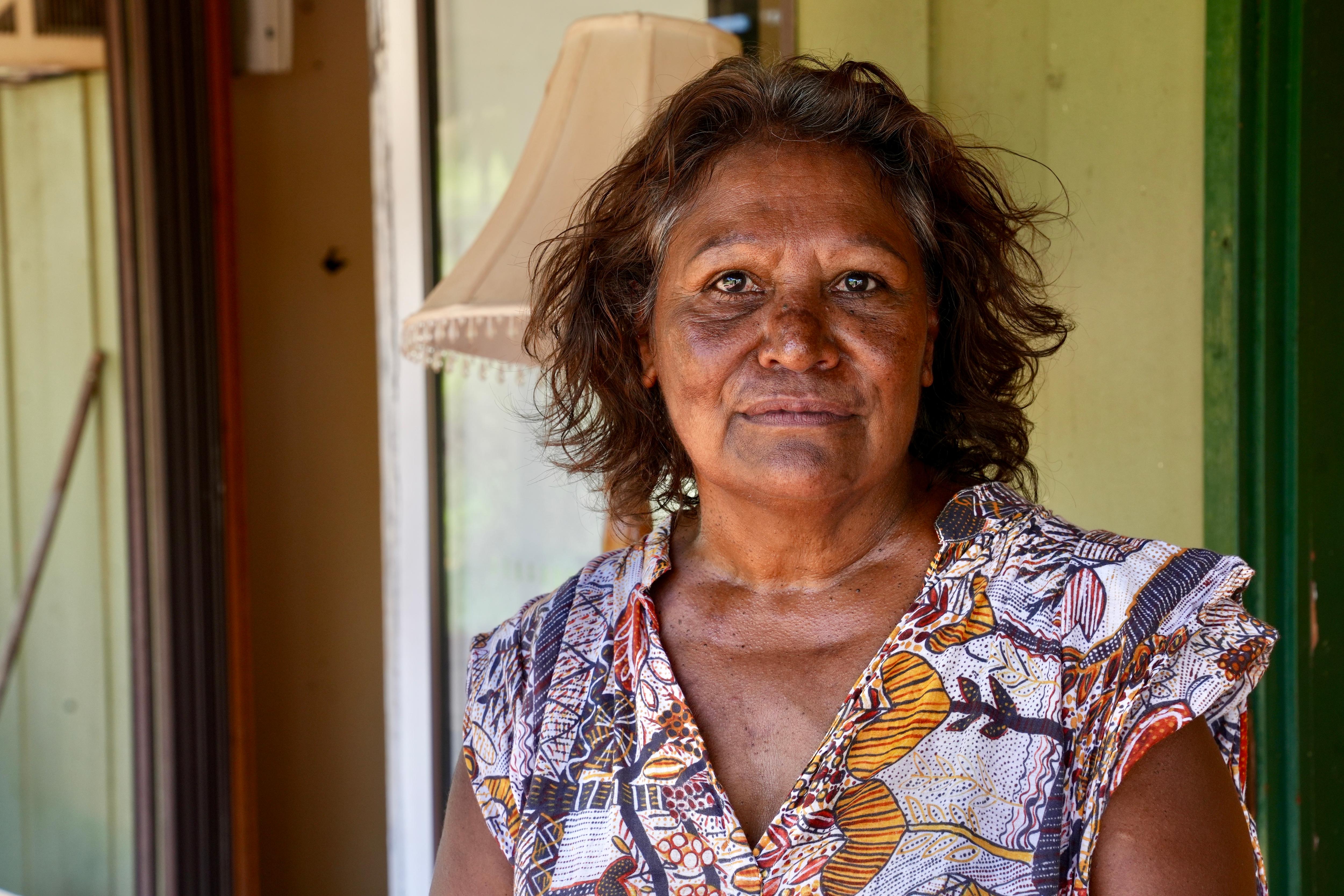 Una anciana aborigen con un vestido colorido se encuentra frente a una puerta