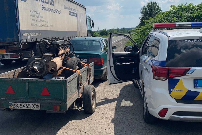 A car with an amber pump in the trailer waits next to the highway.