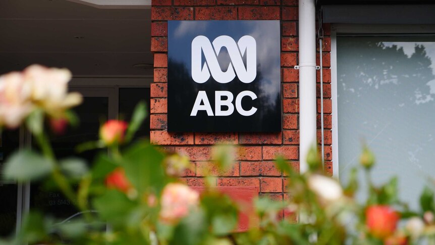 A black and white ABC logo on a brick building with out of focus red and orange roses in the front.