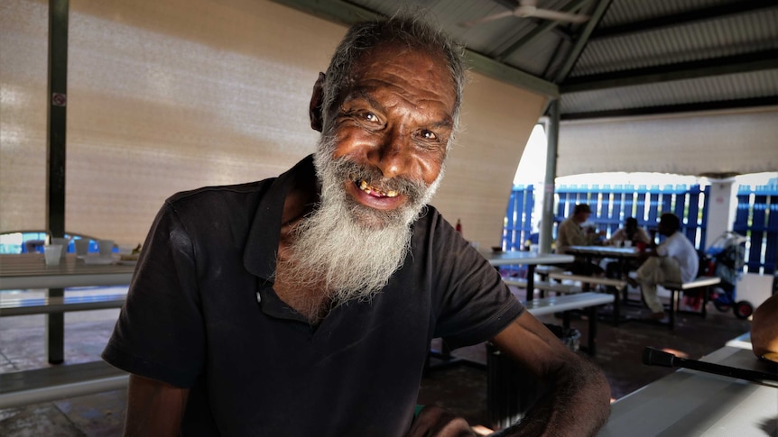 Under a lean-to roof. Long aluminium tables. Morning light. Man with beard looking at camera smiling