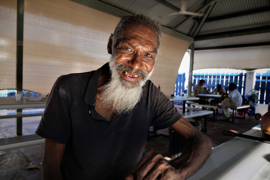 Under a lean-to roof. Long aluminium tables. Morning light. Man with beard looking at camera smiling