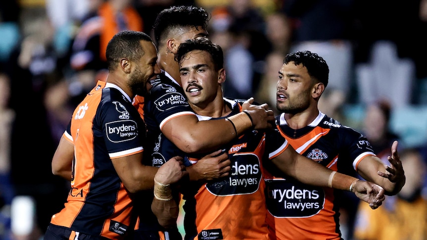 Four Wests Tigers NRL players embrace as they celebrate a try.