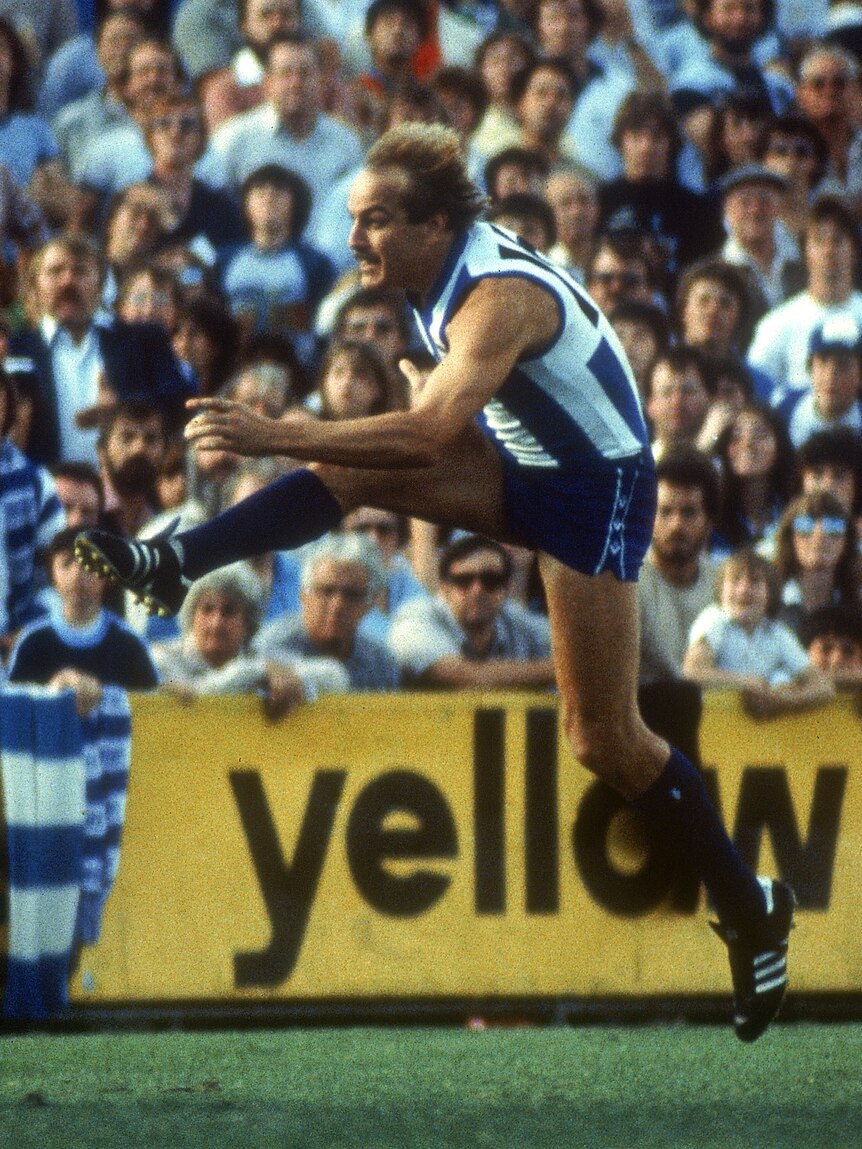 North Melbourne VFL player Malcolm Blight is airborne as he completes a big kick downfield during a match. 