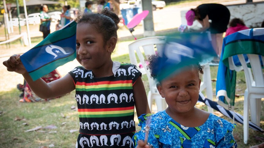 Two girls waving Torres Strait Islander flags at Flag Day celebrations on Thursday Island.
