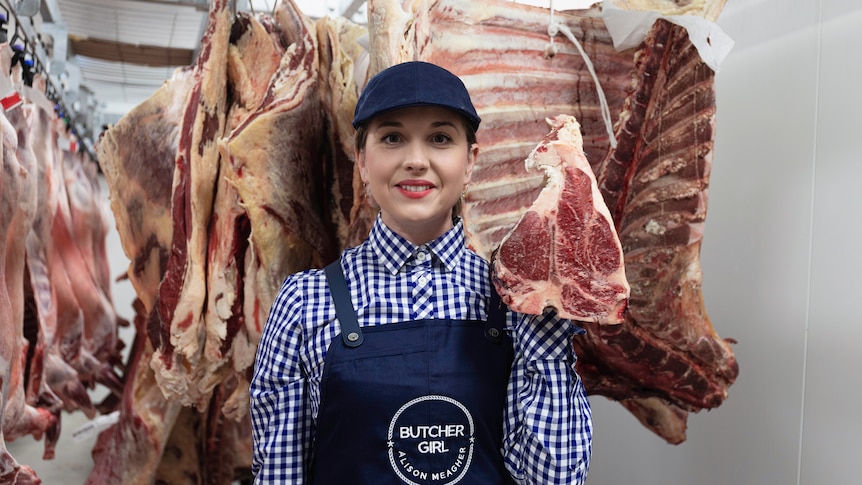 Women smiles at camera with meat carcus' hanging behind her