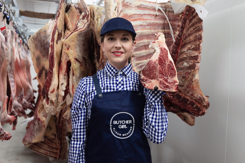 Women smiles at camera with meat carcus' hanging behind her