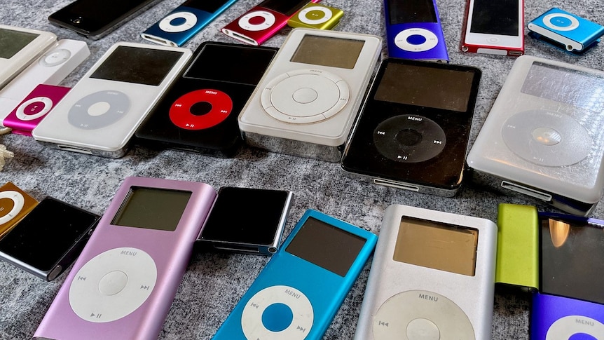 A collection of various models of Apple iPod from throughout the years, lying on a grey surface