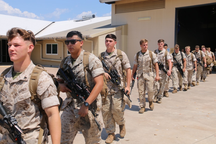 US soldiers march in a line out of an aircraft hanger onto the tarmac.