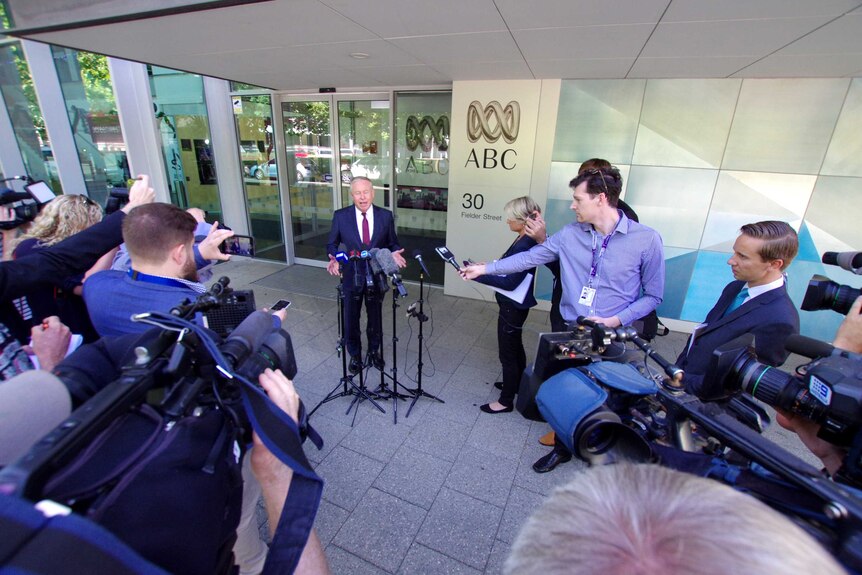 A mna in a suit is questioned by journalists outside an ABC building.
