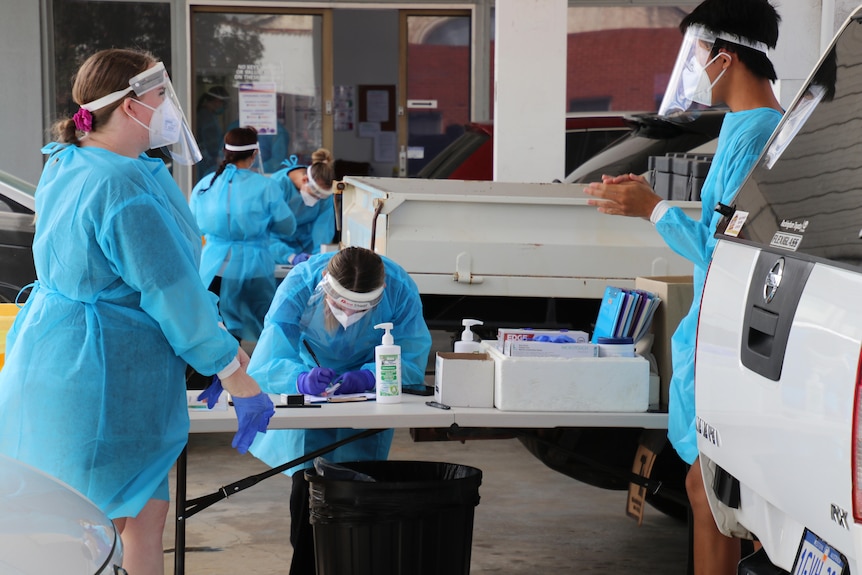 Staff wearing PPE stand in a drive-through COVID testing clinic.