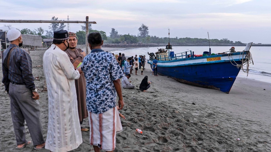 Several men stand on a beach looking at a boat.