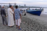 Several men stand on a beach looking at a boat.