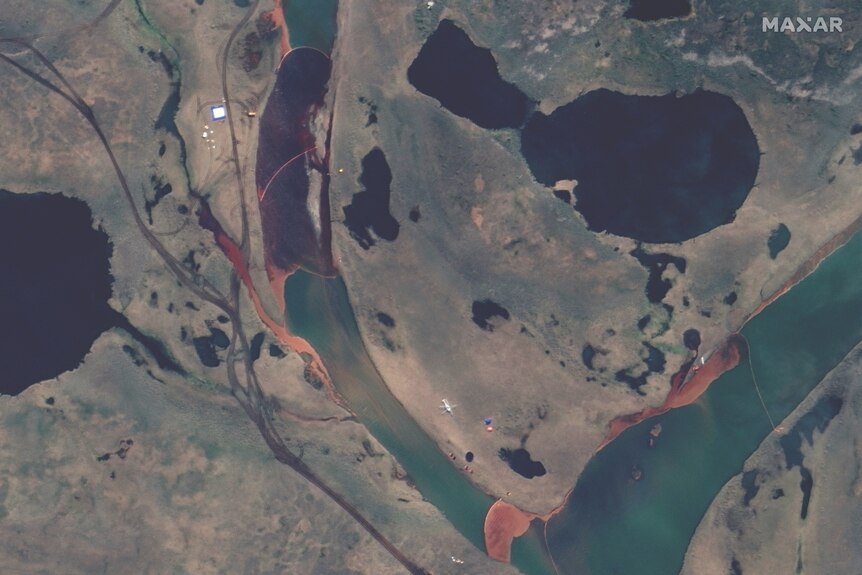 A satellite photo shows a large brown oil slick is visible in a river.