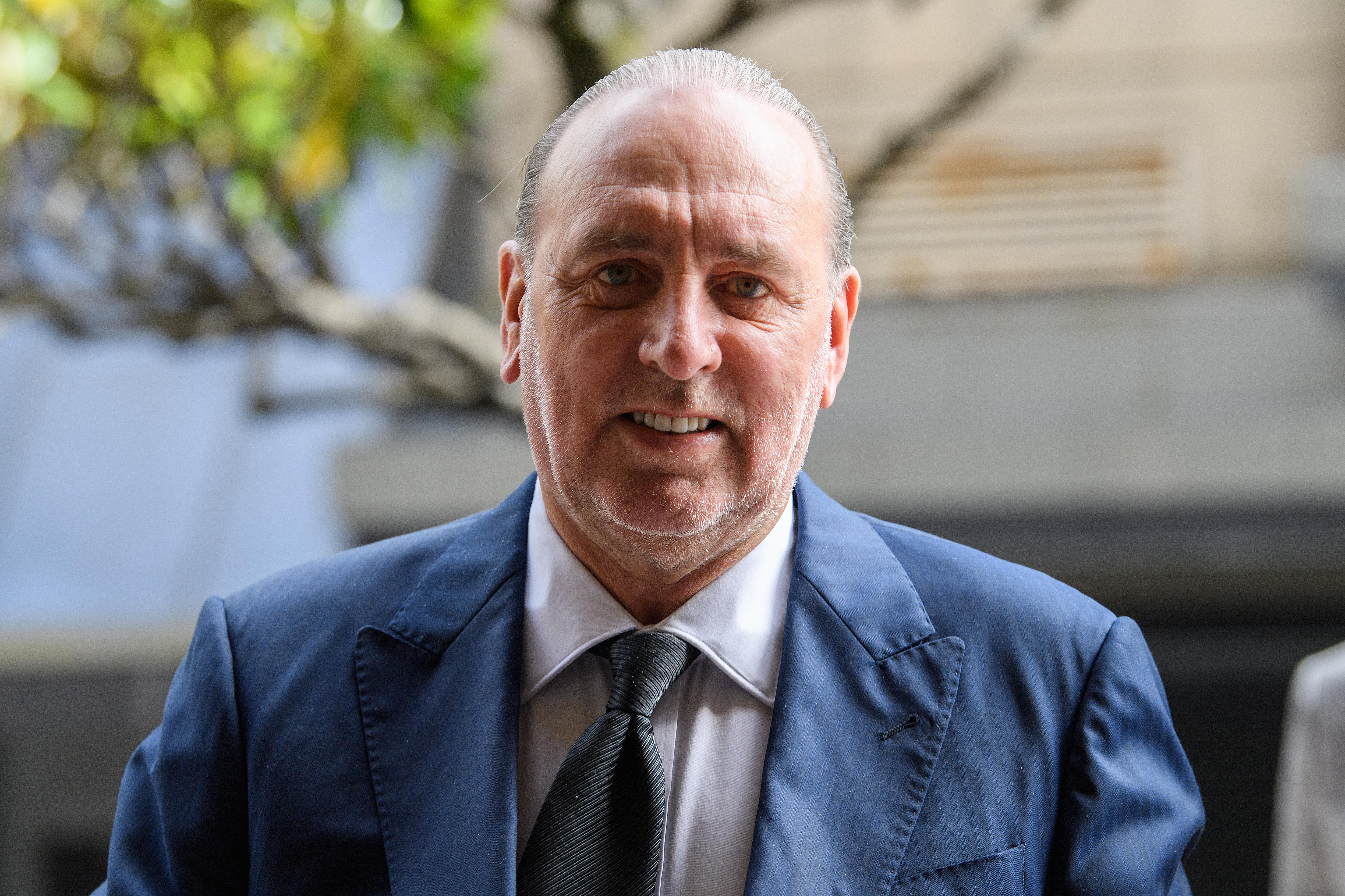 A man wearing a suit and tie stares towards the camera