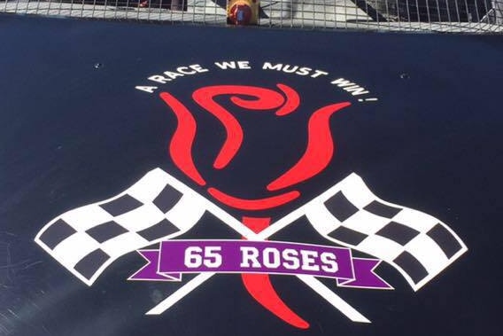 SIgn painted on a dark blue car bonnet of red rose and two racing finish flags, words 65 rosese 