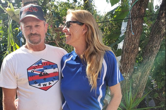 A man and a woman stand in a backyard smiling.