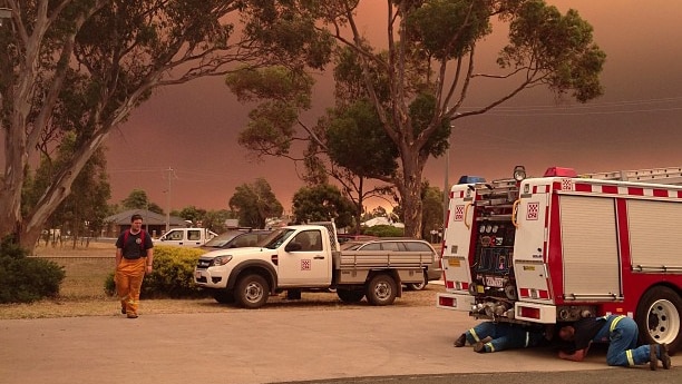 Members of the Churchill Fire Brigade work on their truck as a bushfire burns in the distance near Heyfield.