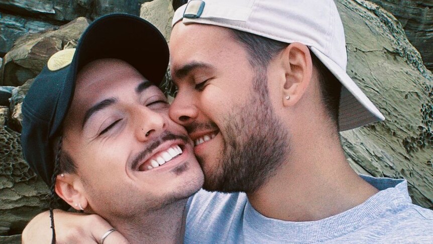 A picture of two men hugging and smiling with their faces pressed together. 