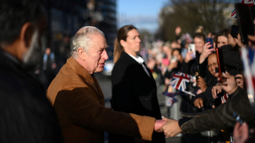 Britain's King Charles shake hands with crowds holding flags. 