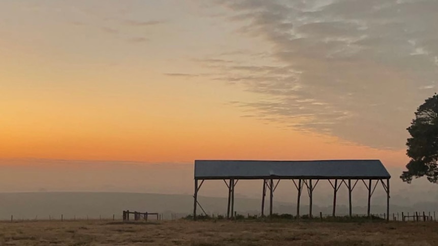 the sun rises over misty hills, with an empty hayshed in the foreground