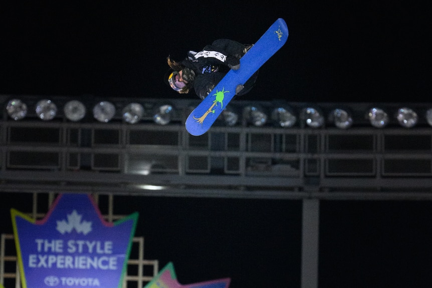 A man holds the side of a blue snowboard in mid air