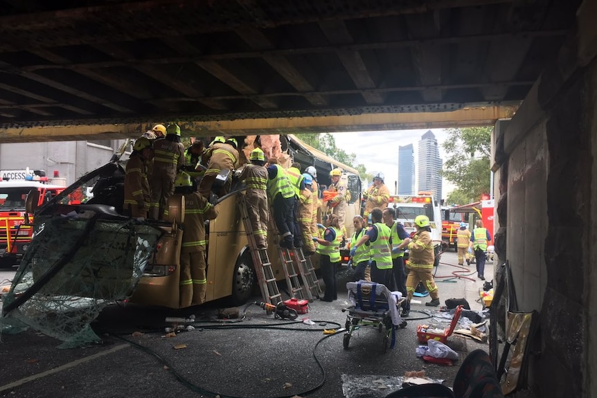 Emergency crews work to free passengers from the bus which is wedged under the bridge.