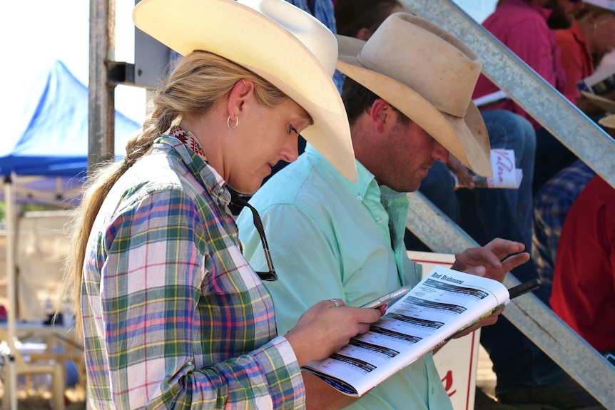 A woman and man wearing staw hats look at program