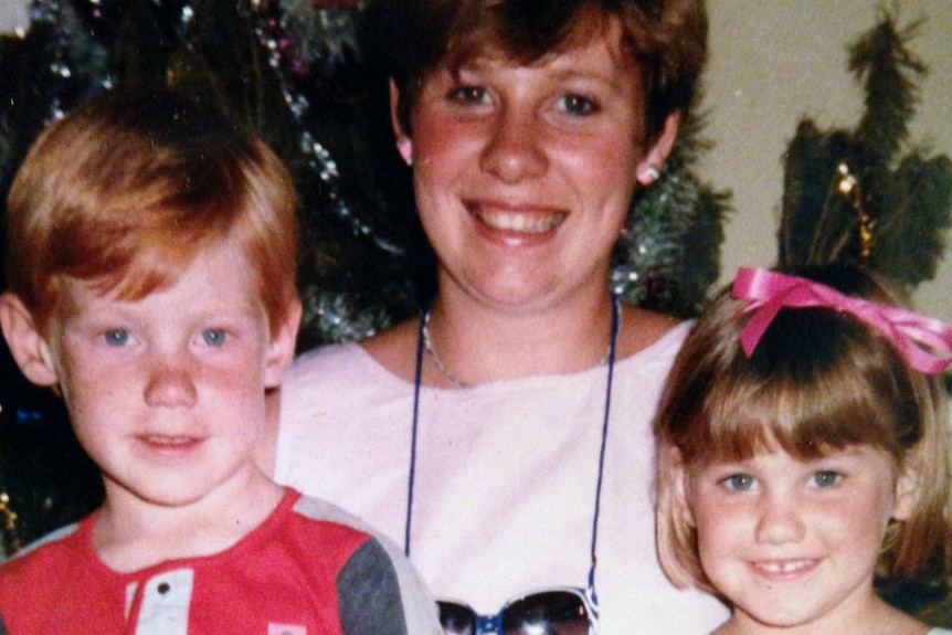 Ursula smiles as she stands between a young boy and a young girl.