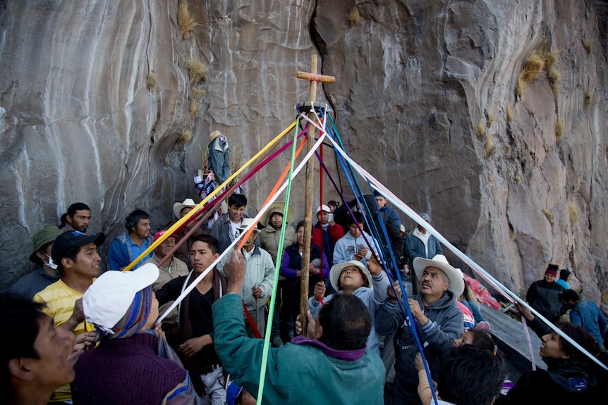 A cross wrapped with ribbons being pulled by a group of people. 