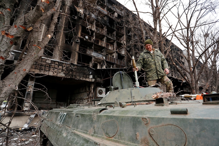 A Russian soldiers hands ordnance to someone inside an armoured vehicle.