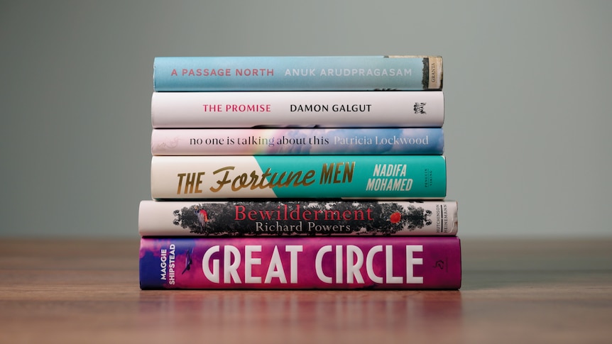 Six books stacked horizontally on wood surface, spines facing camera.