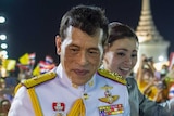 Thailand's King smiles for crowds taking pictures on their phones as queen waves in background.