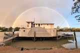 A steamboat sits on a river bank, with a rainbow in the background.