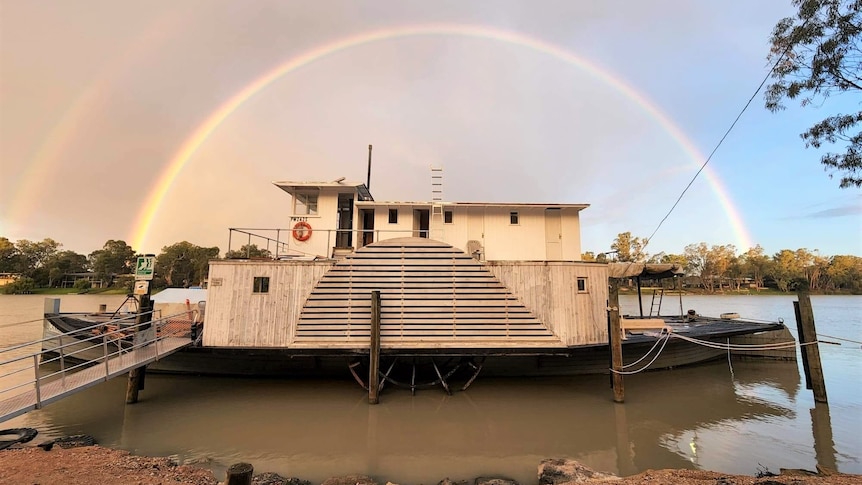 A steamboat sits on a river bank, with a rainbow in the background.