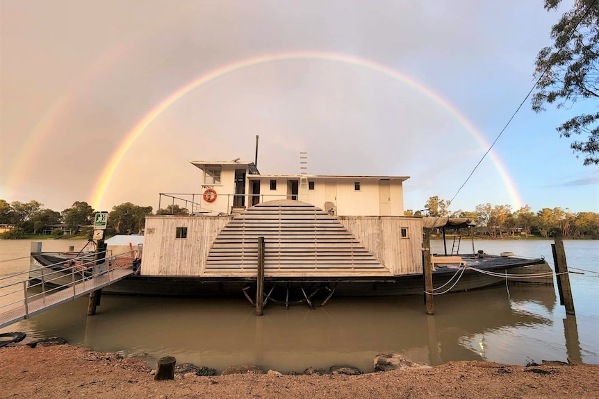 A steamship sits on a riverbank, with a rainbow in the background.