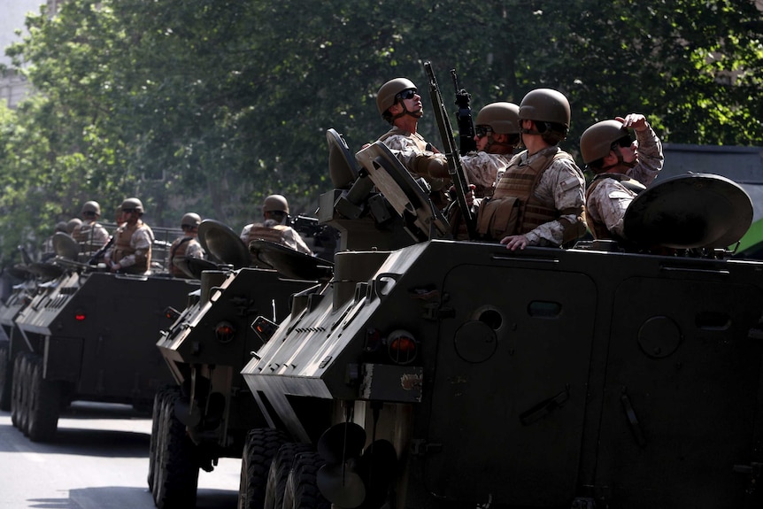 Army soldiers with guns and helmets ride in tanks along the streets