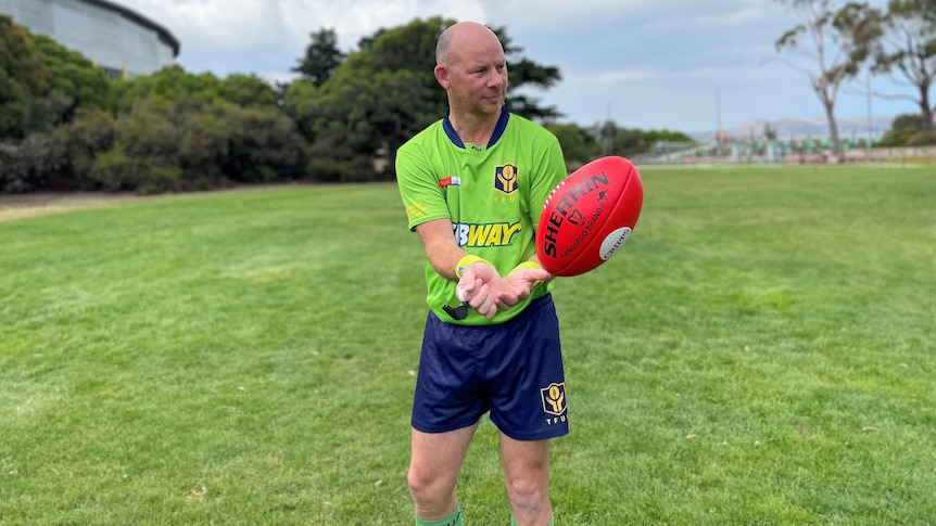 A man wearing an aussie rules umpire's uniform handballs a football