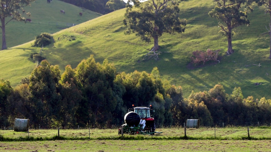 Green pastures with bailed plastic covered hay and a small red tractor, with green hills and trees in background