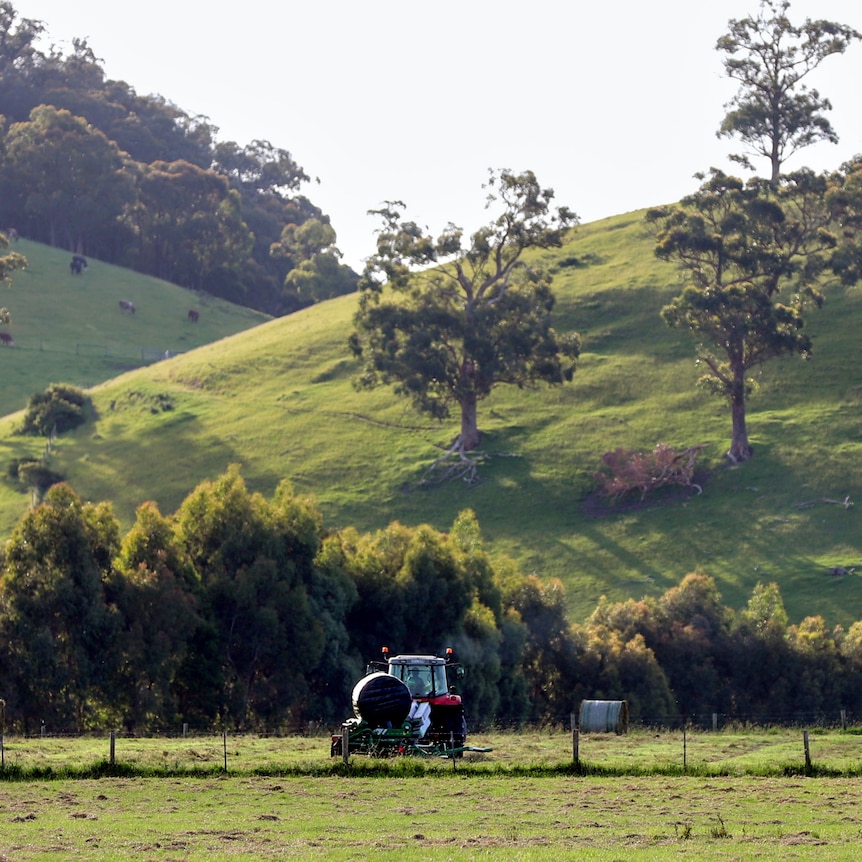 Green pastures with bailed plastic covered hay and a small red tractor, with green hills and trees in background