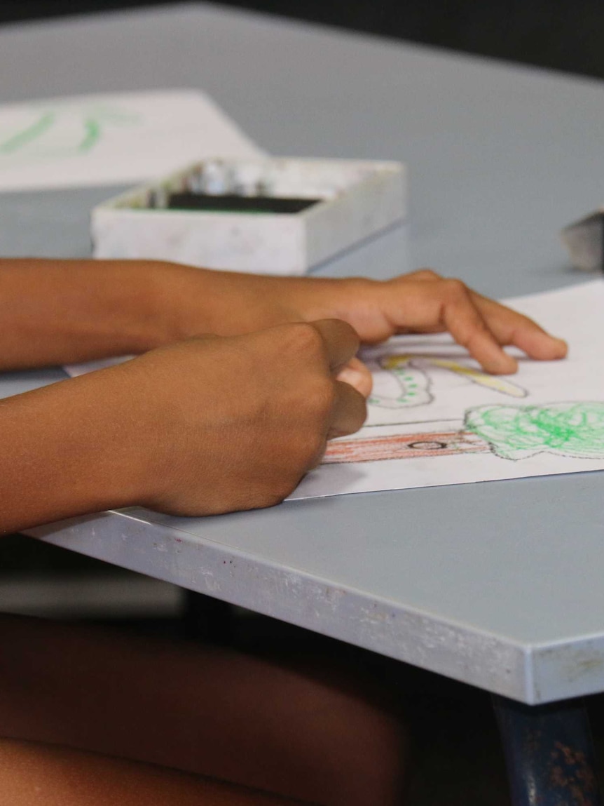 A young Aboriginal student's hands on a school table.
