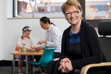 A woman sitting on a chair with a woman and child in the background.