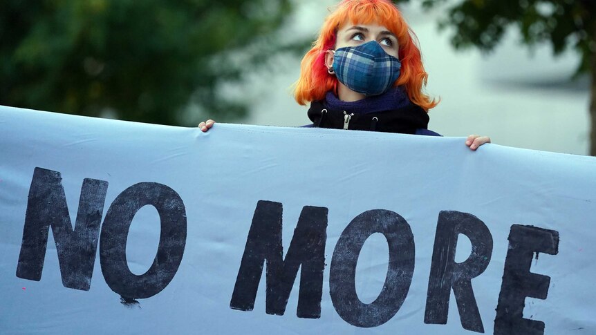 A person with orange hair holds up a sign saying 'no more' at the Glasgow climate conference