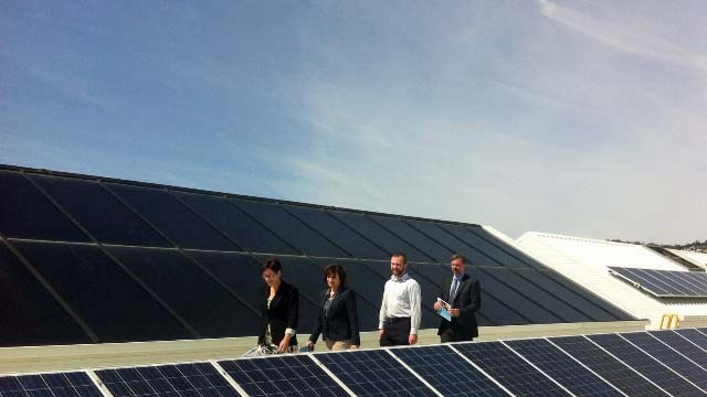 Climate Change Minister Cassy O'Connor (l) walks with industry leaders on a solar panel roof.