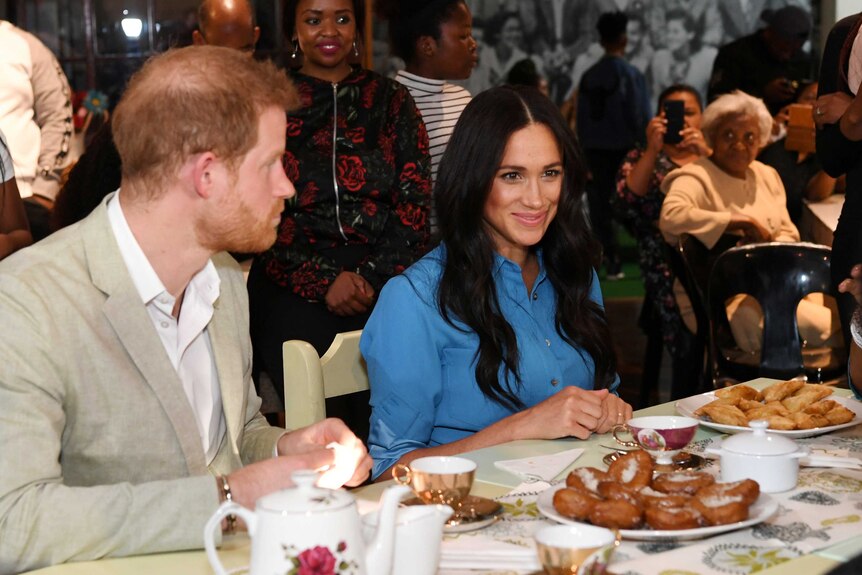 Prince Harry and Meghan are seated at a table with tea and food in front of them
