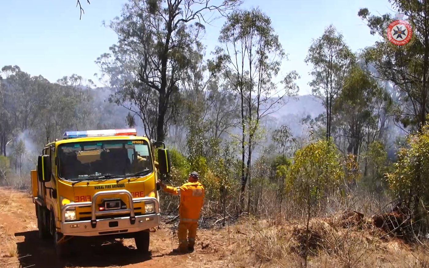 A firetruck on a hill with a fireman looking out into smoke in the distance