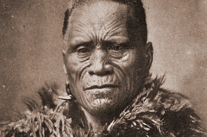 An archival photo of a Maori leader with facial tattoos, wearing a feathered wrap.