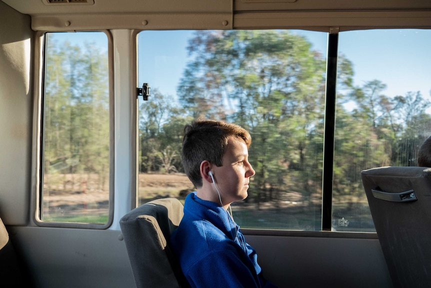 A student wears headphones on a bus as the countryside blurs in the background