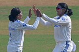 Two women in cricket whites high five 