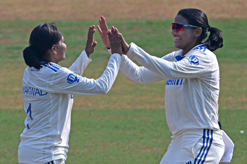 Two women in cricket whites high five 